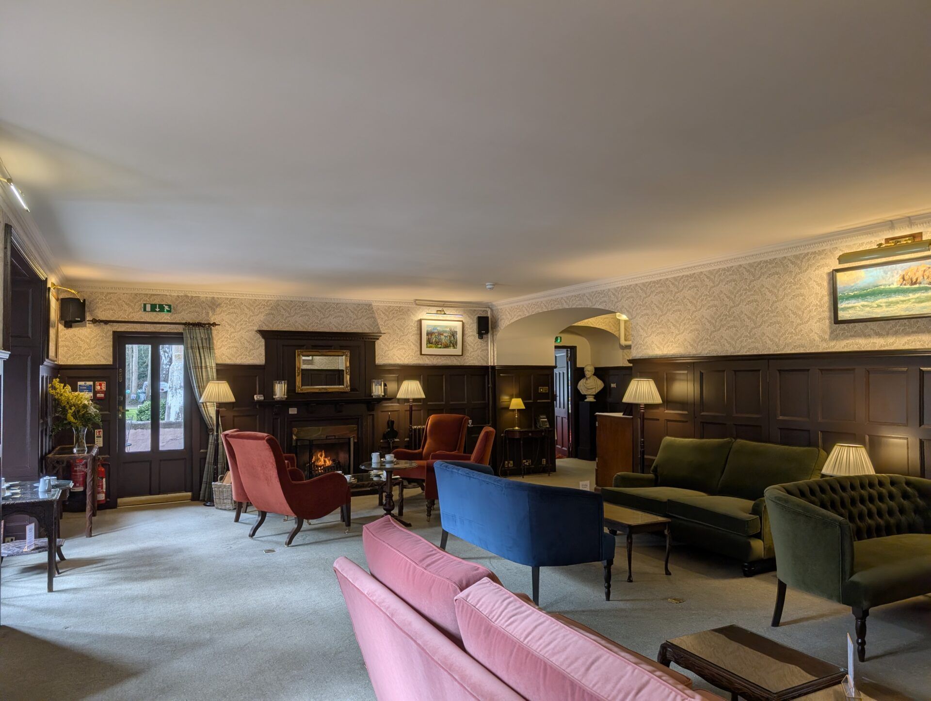 PXL_20260321_125311471 Spacious Bunchrew House Hotel lounge featuring velvet sofas in pink, blue, and olive green arranged near a fireplace.