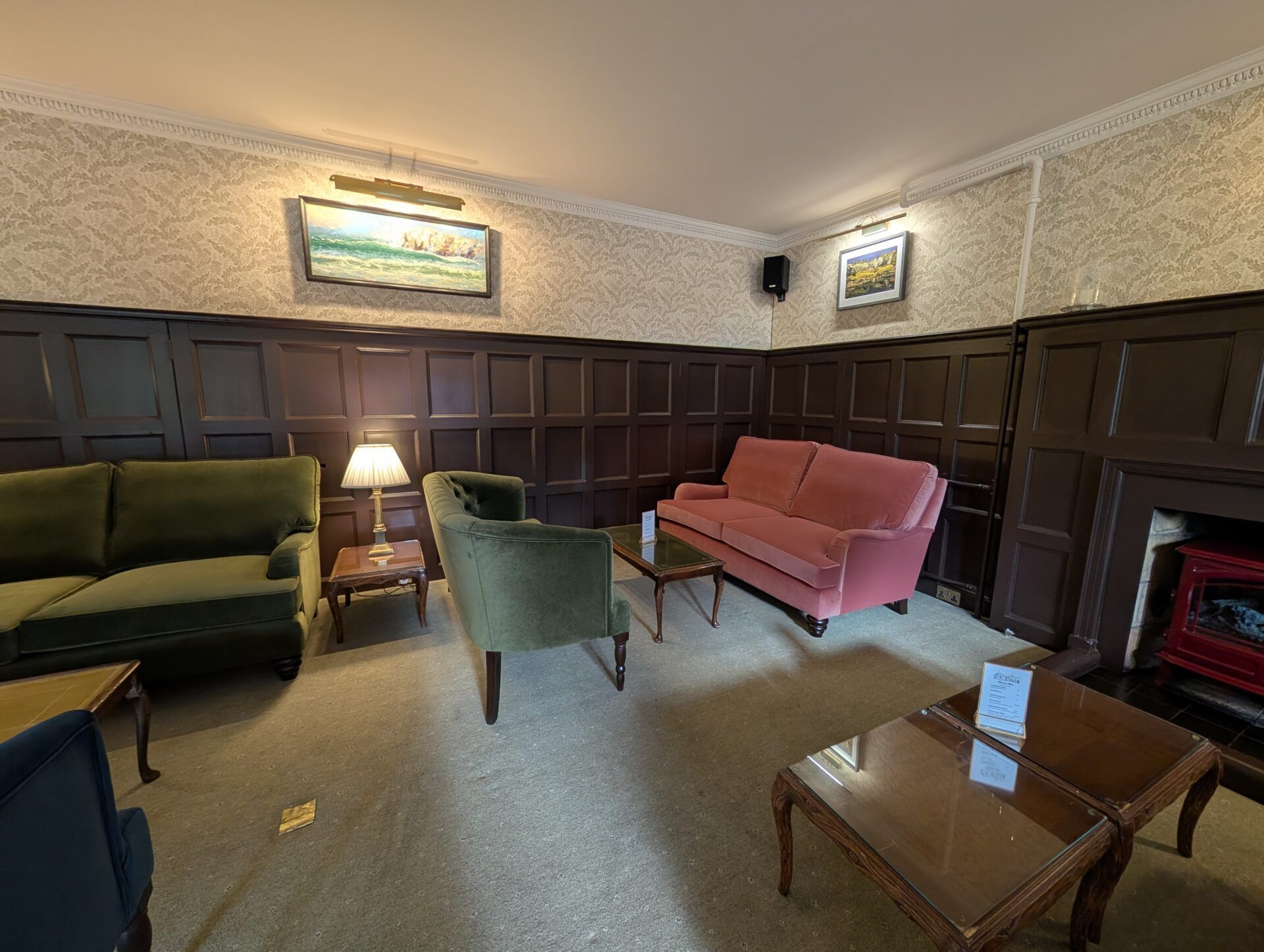 PXL_20260321_125344411 Dark wood wainscoting frames olive green sofas and a coral couch, accented by wall-mounted landscape paintings.