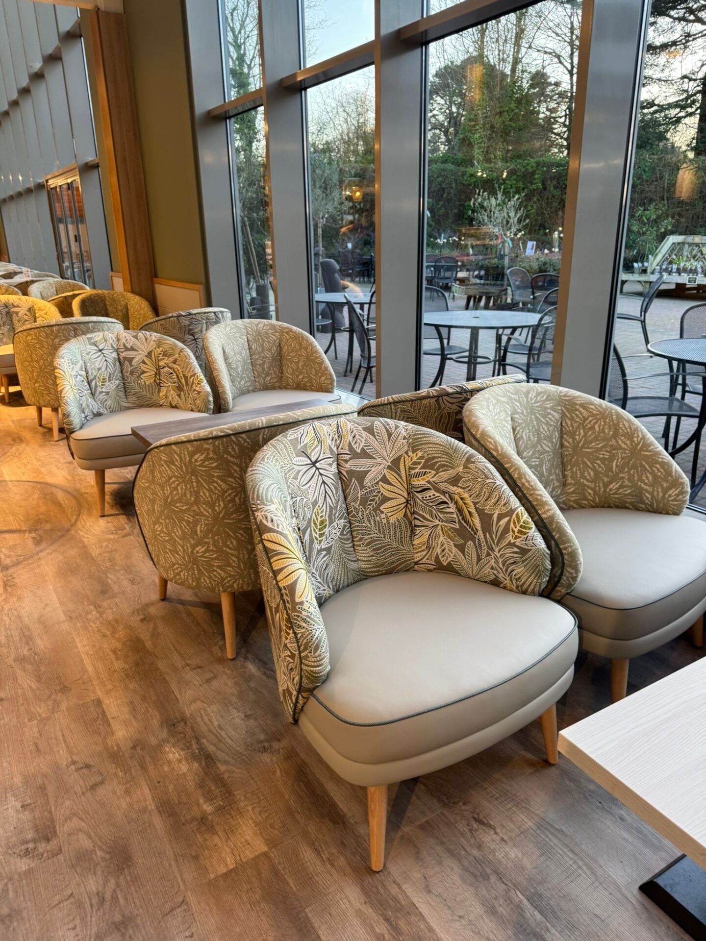 Haskins Garden Centre 3 Curved armchairs with botanical leaf print backs and solid grey seats arranged by floor-to-ceiling windows.
