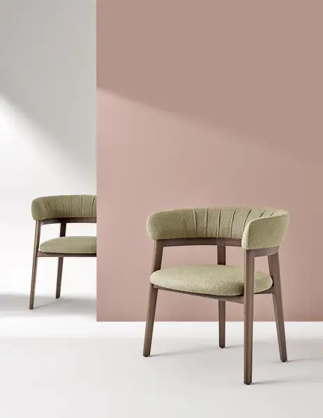 Cora Armchair pair shown in sage green textured fabric with ribbed back detailing and a dark wood base against a pink wall.