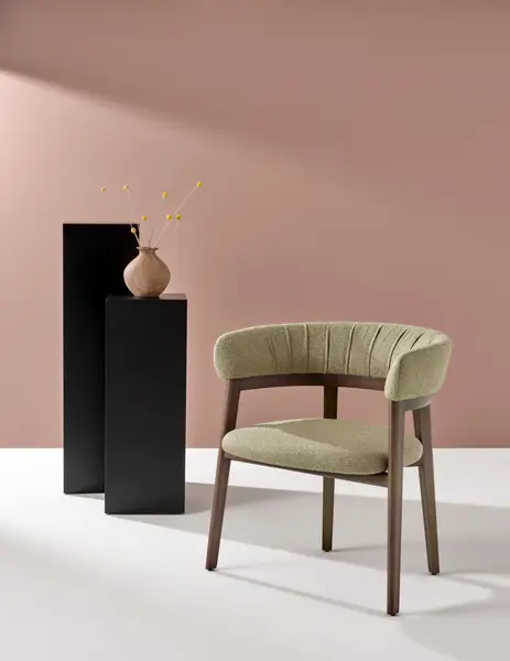 Cora Armchair in light green textured upholstery with a dark wooden frame, placed beside two black pedestals.
