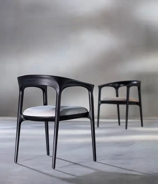Rear view of two Fau Armchairs featuring black wooden frames and light upholstered seats set against a grey background.
