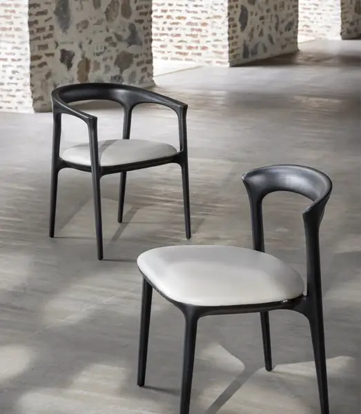 Close-up perspective of two Fau Armchairs featuring dark wood frames and soft cream seats positioned in a bright hall.