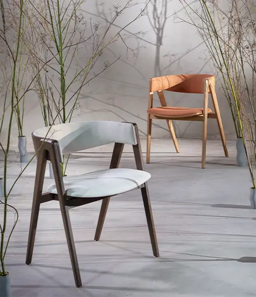 Two Gala W Armchairs in white and terracotta upholstery with wooden frames, displayed in a minimalist botanical setting.