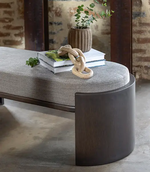 Close-up of the Hug Bench showing a grey upholstered seat, curved dark wooden base, and decorative styling accessories.