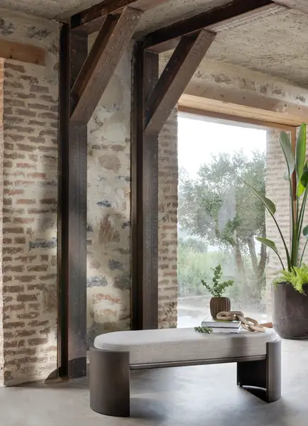 Hug Bench with beige upholstered top and curved dark wood base positioned against a rustic brick and timber interior.