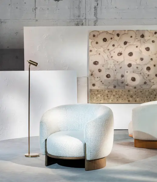 Close-up of the Hug Lounge Chair with soft white fabric, set beside a floor lamp in a contemporary gallery space.