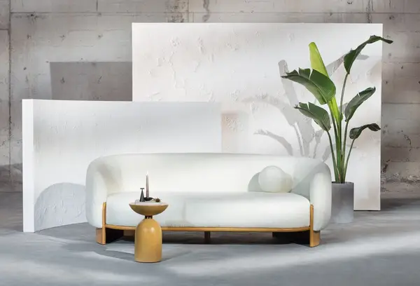 Hug Sofa showcased in a minimalist room with a mustard side table and indoor plant against abstract white panels.