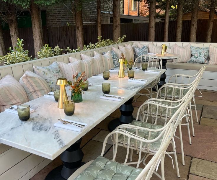 the Victoria3 White metal chairs with patterned sage seat cushions surround long marble tables on a private pub garden patio.