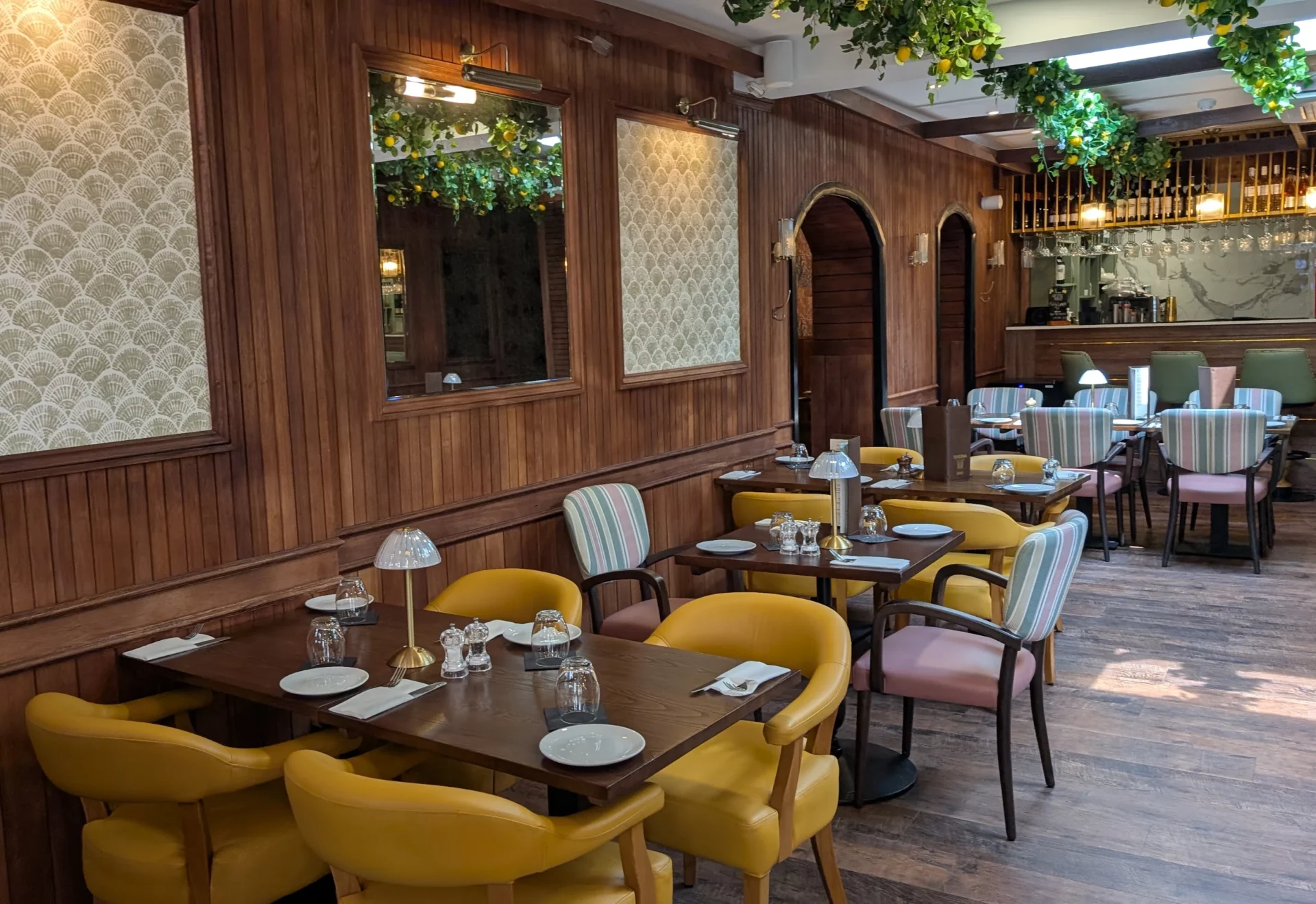 Mustard-yellow armchairs surround dark wood tables in a dining room decorated with scalloped patterns and faux greenery.