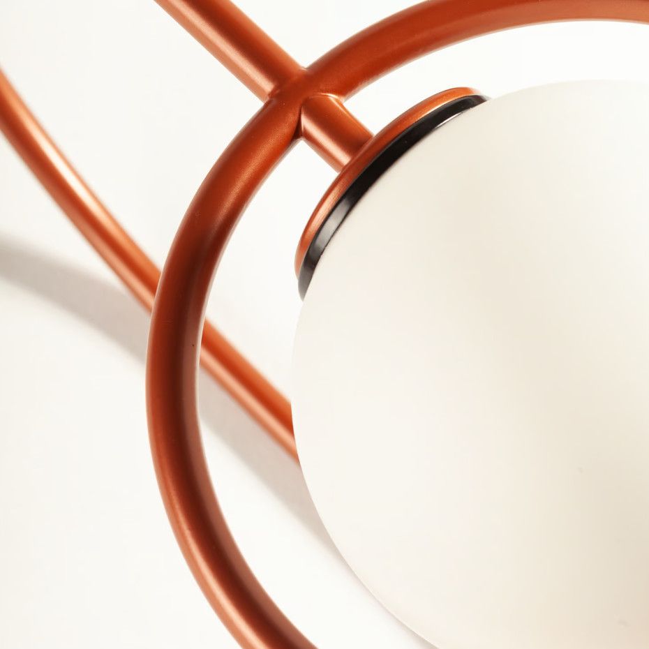 Detail view of the Frame Wall Light showing the spherical glass shade nestled within a sleek, burnt-orange metal frame.