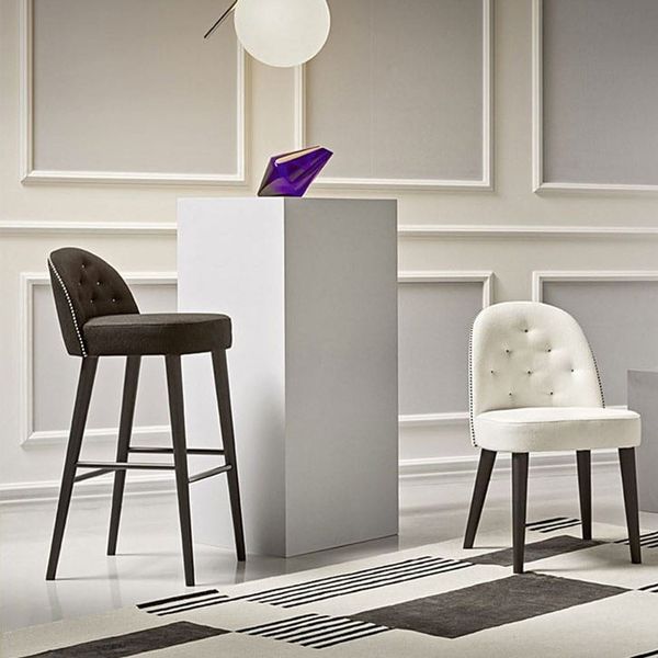 Carmen Barstool in dark charcoal fabric with tufted detailing, positioned next to a matching white dining chair.