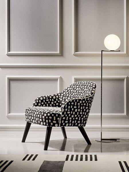 Side view of a Carmen lounge chair featuring patterned fabric, espresso wood legs, and a glowing globe floor lamp nearby.