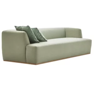 Estival sofa in sage green fabric with a low-profile wooden base and two matching decorative cushions, isolated.