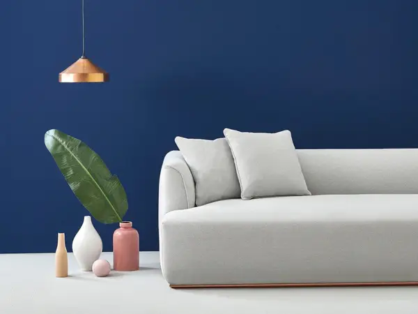 Estival sofa with light grey upholstery, set against a dark blue wall with minimalist vases and a copper pendant light.