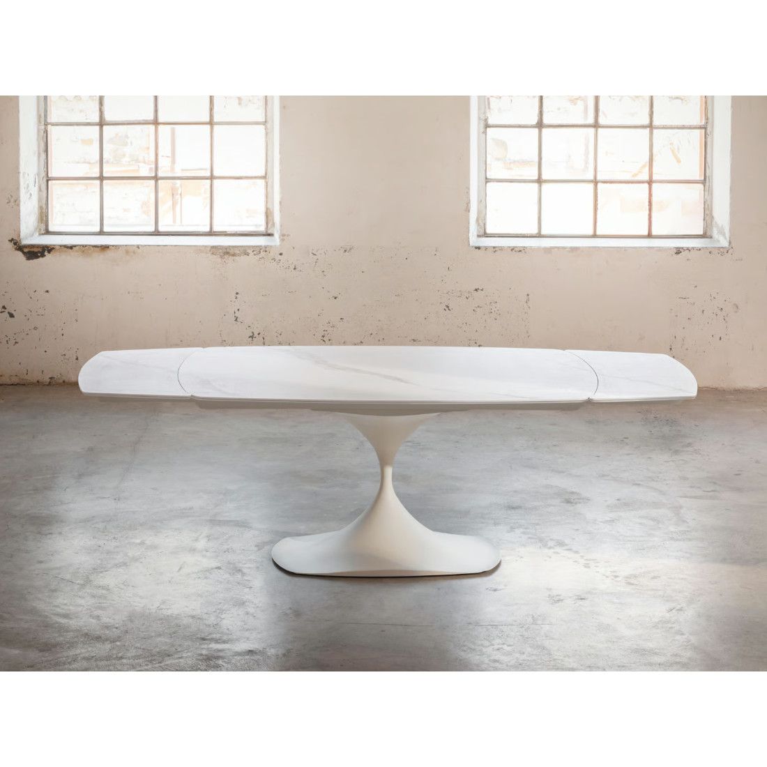 Front view of the Leo Extendable Dining Table with white ceramic surface and matching pedestal base in an industrial loft.