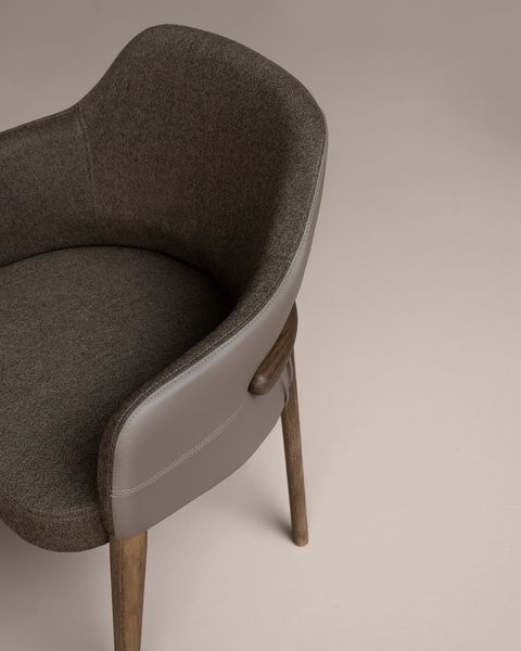 Side angle of the Trench Armchair with grey leather exterior, dark wool seat, and curved wooden legs on a plain background.