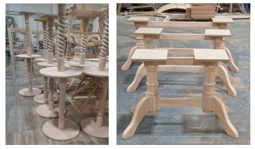 Spindly wooden table bases with barley twist columns sit beside larger trestle-style bases on a workshop floor.
