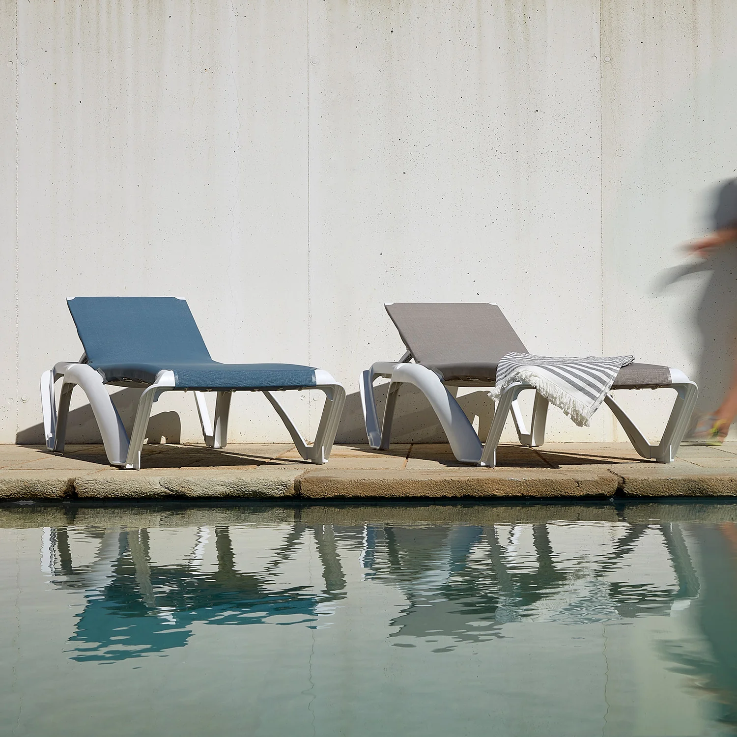 Front view of two Mimi sun loungers with white polypropylene frames beside a pool, featuring blue and grey seating.