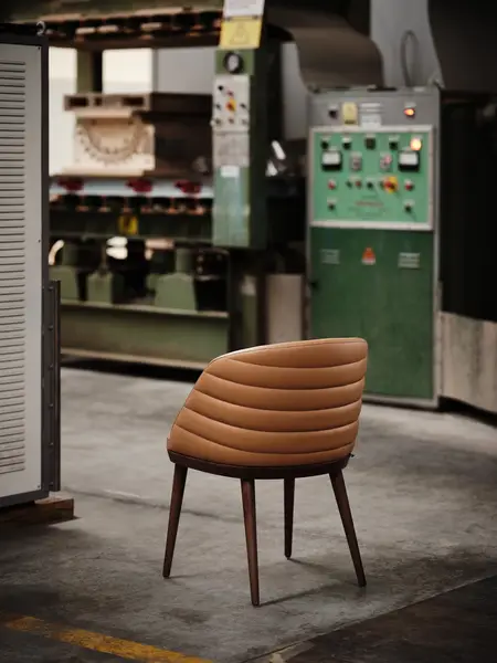 Amara armchair with tan horizontal-stitched upholstered back and dark wooden legs, viewed from the rear in a workshop.