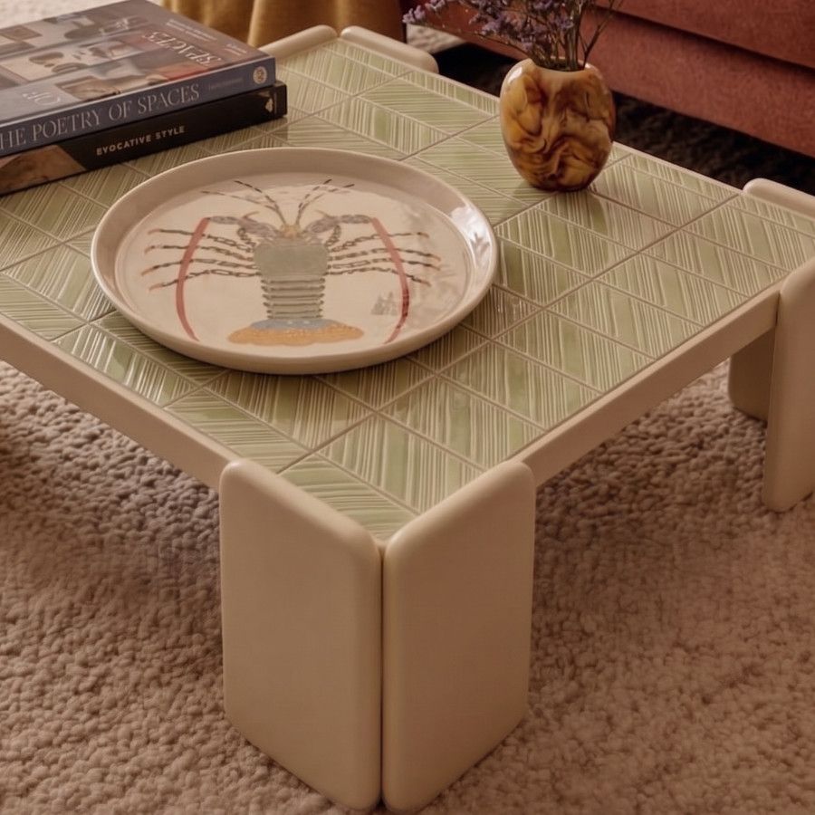 Close-up of a Chess Coffee Table featuring a sage green tiled surface, styled with a lobster tray, books, and a vase.