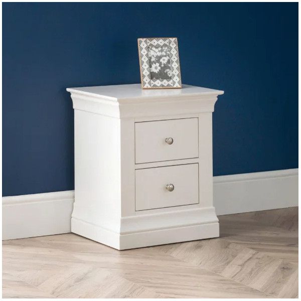 Angled view of a white Camille bedside table with a patterned picture frame, set against a deep blue wall.