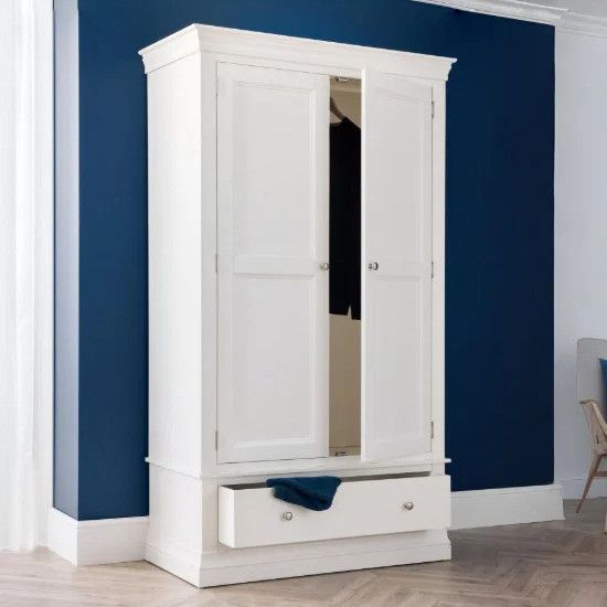 Angled view of the Camille wardrobe showing an open door and partially pulled-out drawer against a navy blue wall.