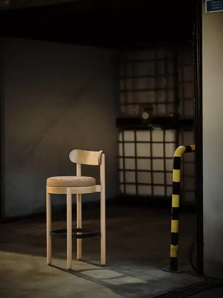 Doris Barstool with light wood frame, upholstered round seat, and curved backrest, shown in a studio setting.