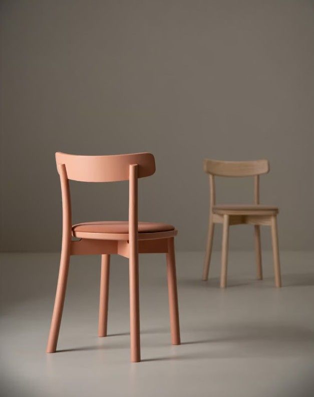 Close-up of a terracotta-colored Fondina W Side Chair with a matching seat pad, set against a blurred light wood version.