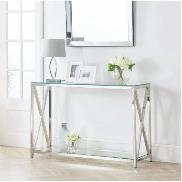 Styled shot of a Miami Console Table with a silver cross-leg base, glass shelves, and decorative home accessories.