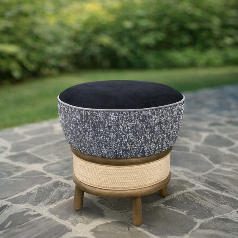 Miko Low Stool featuring a black velvet seat, gray patterned side, and natural rattan base on a stone patio.