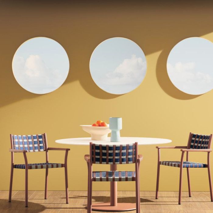 Three Nuova Guinea armchairs with terracotta frames and navy-white woven seats arranged around a central dining table.