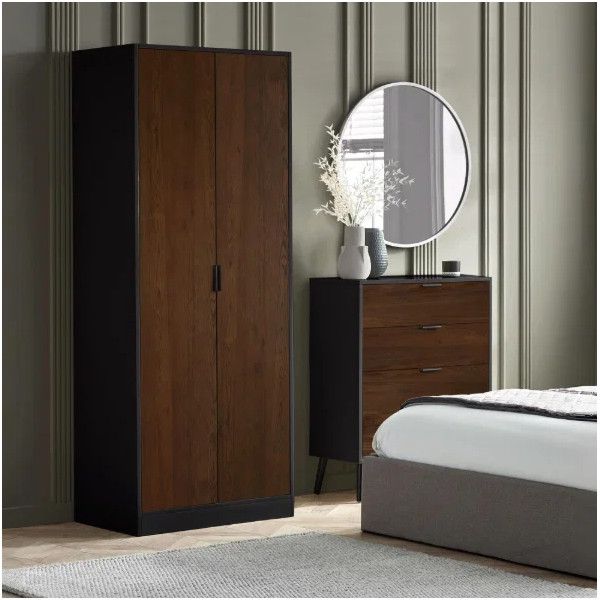 Alba wardrobe in dark oak wood with black trim, standing beside a matching chest of drawers in a stylish bedroom.