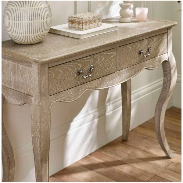 Camille Console Table with two drawers, decorative items on top, and curved legs in a light wood finish.