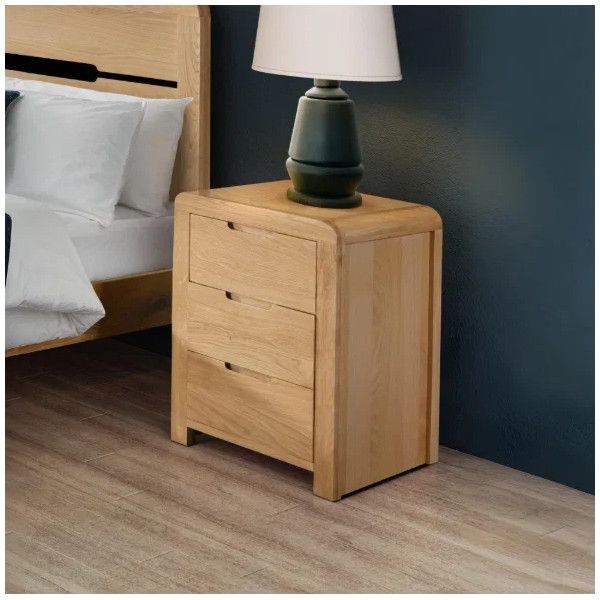 Close-up of the Curve Bedside cabinet featuring three closed drawers and a table lamp, set in a modern bedroom interior.