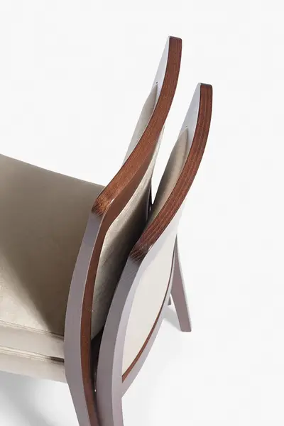 Close-up profile of stacked Dora Stacking Side Chairs showing curved wooden frames and soft beige upholstered seats.
