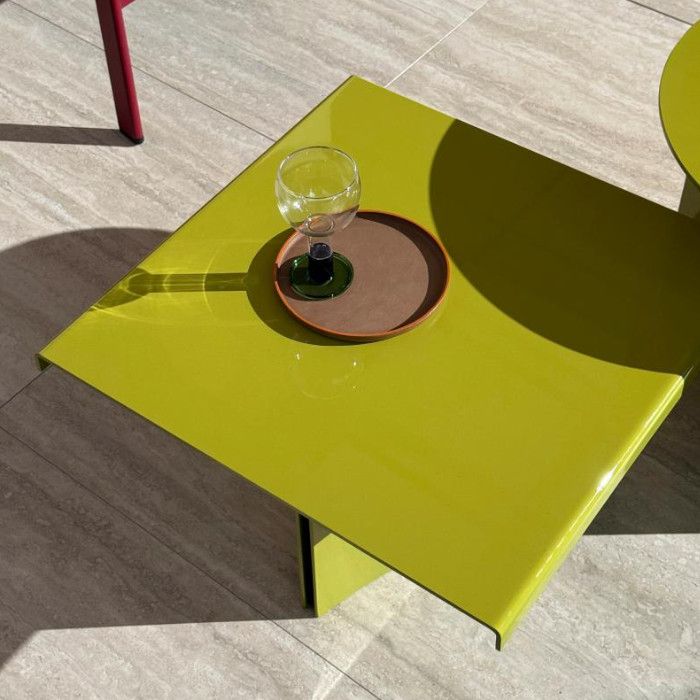 Top-down view of a glossy chartreuse Estratto coffee table, featuring a small tray and wine glass on the metal surface.