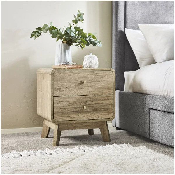 Ingrid bedside table styled next to a grey bed with eucalyptus leaves in a vase and modern wooden frame design.