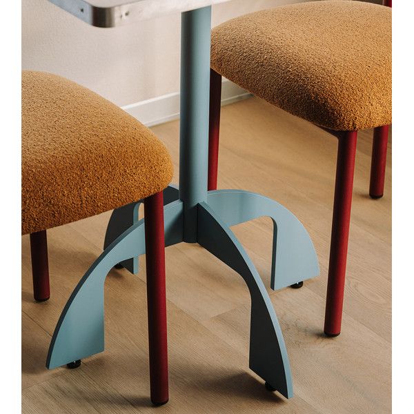 Close-up of a blue Noru dining table base with arched metal legs, positioned between two textured amber chairs.