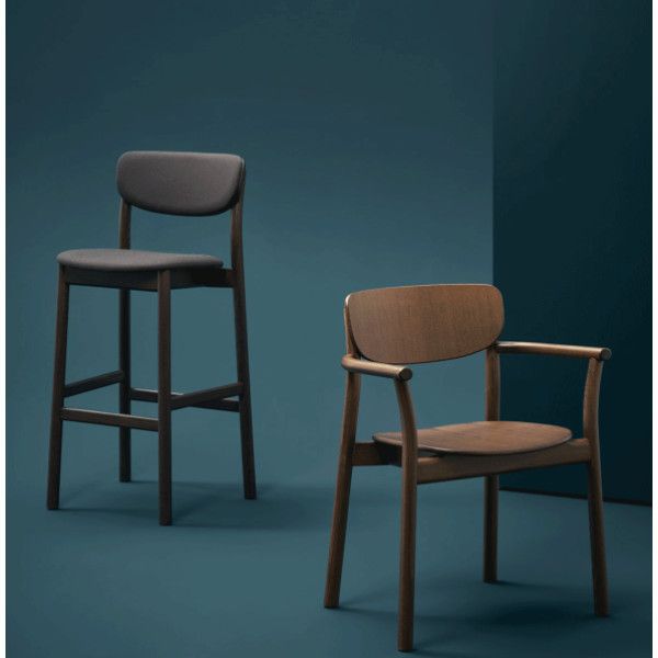 Wooden Zelda armchair with a curved backrest beside a tall bar stool, both in a rich dark finish on a teal background.
