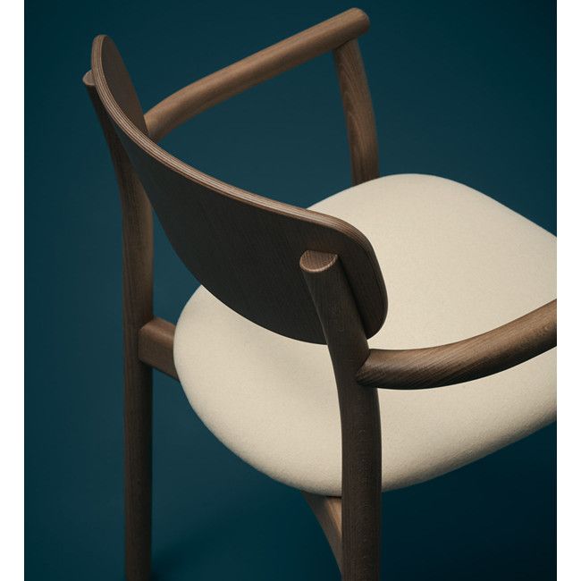 Close-up rear view of the Zelda armchair featuring a curved wooden backrest and cream upholstered seat against teal.