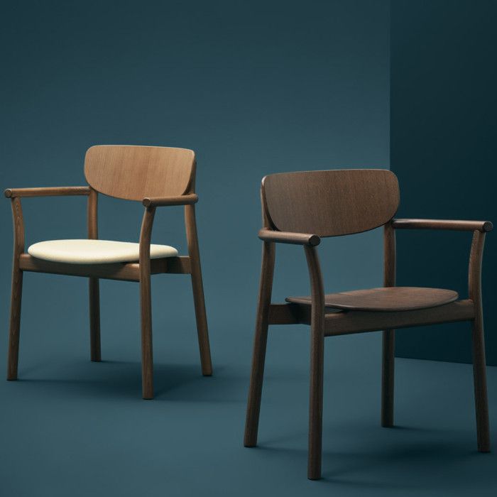 Two Zelda armchairs in dark wood, one with a cream seat pad and one with a matching wooden seat, against a dark teal wall.