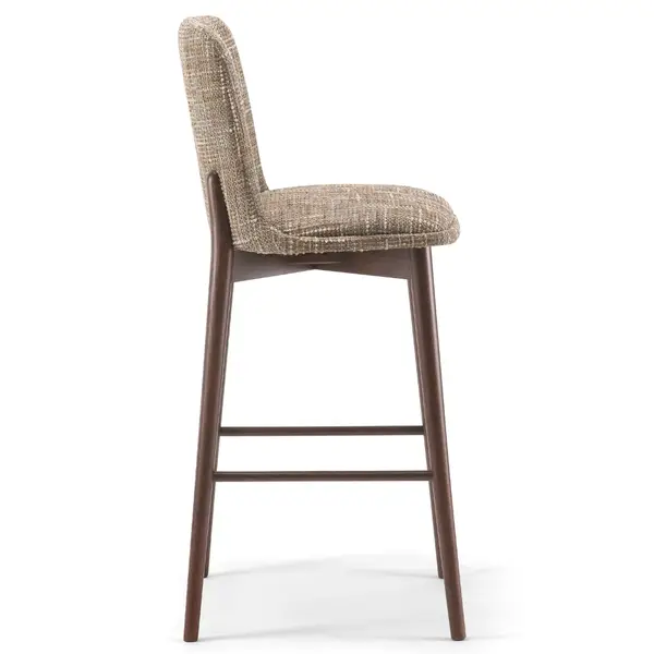Side profile of the Celine Barstool showing its beige upholstered seat and backrest with a dark wooden frame and footrest.